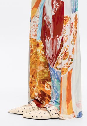 Multicolored maxi dress with floral and abstract patterns; beige pointed-toe shoes featuring silver studs and a buckle strap.