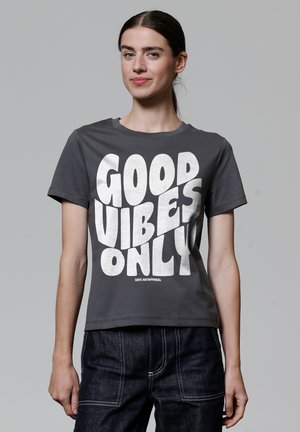 Grijze katoenen t-shirt met korte mouwen, voorzien van een grote witte grafische tekst "GOOD VIBES ONLY" in een vet, speels lettertype.