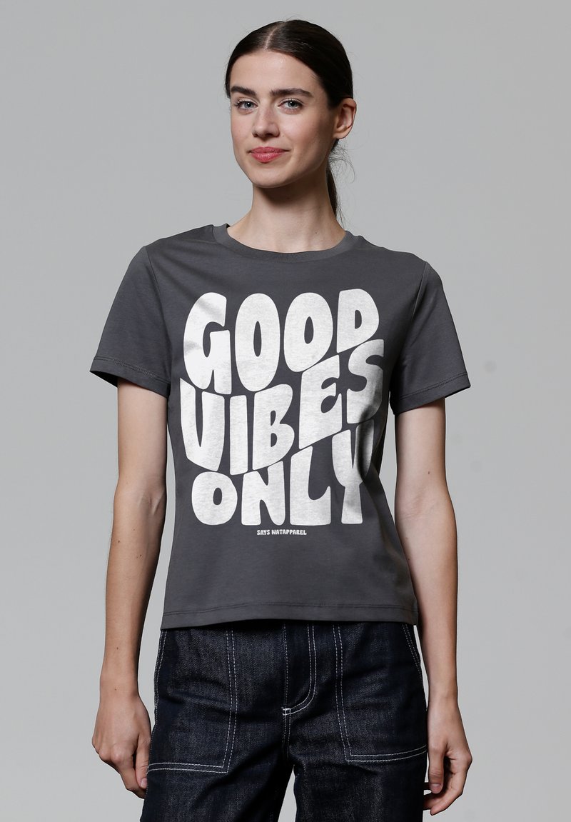 Grijze katoenen t-shirt met korte mouwen, voorzien van een grote witte grafische tekst "GOOD VIBES ONLY" in een vet, speels lettertype.