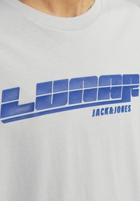 Pilkas medvilninis marškinėliai su ryškiu mėlynu užrašu "LUNAR" ir po juo, smulkiu šriftu, užrašu "JACK&JONES".