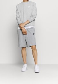 Grå Nike-tröja med långa ärmar och logotyp, kombinerad med grå shorts och vita sneakers med texturerade detaljer och logotypaccenter.