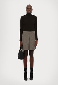 Svart ribbet turtleneck, grå rutete skjørt med frontpleat, svarte hælankler støvler, og en liten svart håndveske med gullakenter.
