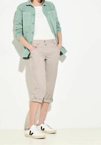 Vaaleanvihreä napillinen paita valkoisen t-paidan päällä, yhdistettynä beigeihin tuulipantalereisiin, joissa on käänteet ja kaksi nappia. Valkoiset tennarit.