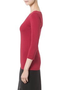 Rode, nauwsluitende top met lange mouwen van gladde stof. Heeft een boothals en driekwartmouwen met een discreet logo op de mouw.