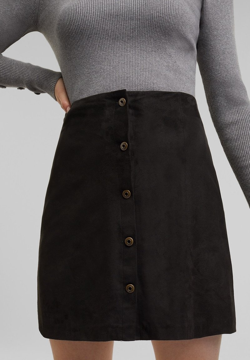 Zwarte suède mini-jurk met zes bruine knopen aan de voorkant, met een gladde textuur en een getailleerd ontwerp. Bovenaan een grijze ribbeltrui.