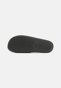 Suela de zapato de goma negra con patrón de agarre texturizado. Presenta un logo en el centro y una forma curvada a lo largo de los bordes. Perfil plano.