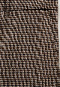 Tissu pied-de-poule marron et noir avec une petite poche et un détail de couture propre.