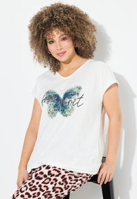 Camiseta blanca con un gráfico de mariposa azul y el texto "espíritu libre". Con mangas cortas y corte relajado. Combinada con pantalones de estampado leopardo rosa.
