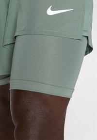 Grüne Sportshorts aus glattem Stoff, mit einem weißen Nike-Logo, einem schlanken Design und einem seitlichen Taschen Detail.