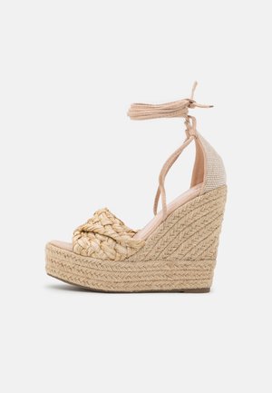Sandales compensées avec un dessus en paille tressée, une bride de cheville beige et une plateforme tissée texturée. La hauteur du talon est prononcée, offrant une élévation.