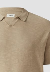 Polo en maille beige à manches courtes avec col en V ouvert et étiquette s.Oliver à l'intérieur du col.