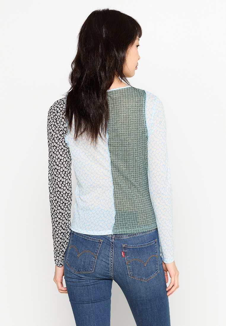 Camisa de manga larga con diseño de patchwork: paneles negros con flores, azul claro y verde texturizado. Hecha de una tela ligera y con patrones.