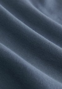 Donkerblauwe stof met een gladde textuur, met fijne ribbels en zachte plooien, die duiden op een lichtgewicht en rekbaar materiaal.