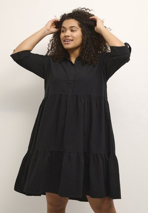 Vestito nero a strati realizzato in tessuto leggero. Presenta una patta con bottoni e maniche lunghe, con una silhouette fluida e una vestibilità rilassata.