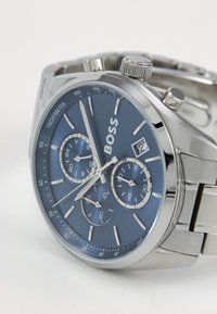Silver stainless steel watch with a blue dial, chronograph sub-dials, date display, and polished accents. Features a tachymetric scale.