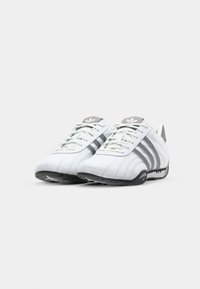 Adidași albi cu accente gri, având un superior din piele netedă, trei dungi laterale și o talpă din cauciuc texturat.