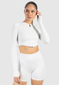 Hvid cropped zip-up langærmet top med ribbet tekstur, parret med højtaljede hvide shorts. Simpelt design, elastisk stof.