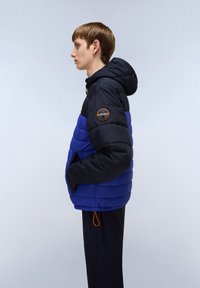 Pudret jakke med et design i navyblå og elektrisk blå farveblok, med hætte, elastisk kant og en rund logo-patch på skulderen.
