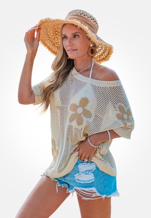 Jersey de punto beige con patrones de flores, combinado con shorts de mezclilla desgastados. Acentuado con un sombrero de paja de ala ancha y pendientes de aro.