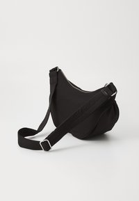 Czarna torba na ramię z tkaniny o zaokrąglonym kształcie, regulowanym paskiem, srebrnym zamkiem błyskawicznym i marszczeniami po jednej stronie.