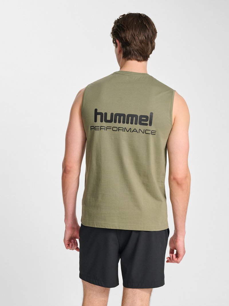 Homme portant un débardeur vert olive avec le texte « hummel PERFORMANCE » dans le dos et un short noir, debout devant un fond uni.