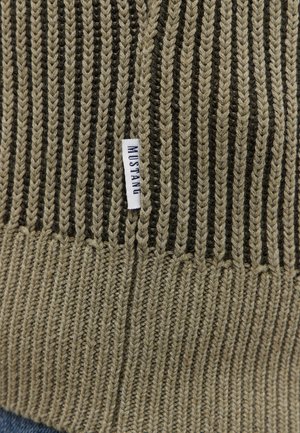 Adītā beanie olīvzaļā un tumši brūnā krāsā ar vertikālu ribu tekstūru. Tam ir mazs balts birku ar uzrakstu "MUSTANG". 