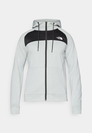 Lys grå hettegenser med glidelås og svart fargeblokkdesign på øvre del foran, med snor i hetten og lommer foran.