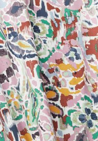 Multikleurige stof met een abstract bloeiend en geometrisch patroon. Prominente kleuren zijn roze, groen, oranje en hints van blauw en bruin.