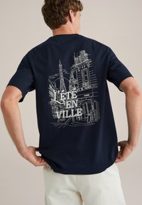 Navy Baumwoll-T-Shirt mit einem weißen Grafikdruck des Eiffelturms und einer Stadtszene sowie dem Text "L’ÉTÉ EN VILLE 1987" auf der Rückseite.