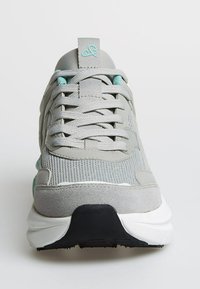 Gray athletic shoe with mesh and suede upper, thick white sole, light blue accents, and crisscrossed laces viewed from the front.