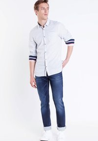 Ljust blå skjorta med en subtil mönstring, marinblå och röda randiga manschetter, kombinerad med mörkblå jeans och vita sneakers.