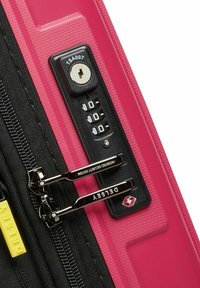 Sezione di valigia rigida rosa con lucchetto approvato TSA e doppia cerniera, con finitura testurizzata e etichetta di branding gialla.