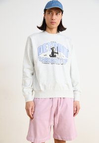 Felpa grigia con stampa grafica che presenta "DETROIT CARHARTT WP" e un personaggio dei cartoni animati, abbinata a pantaloni corti di colore rosa chiaro.