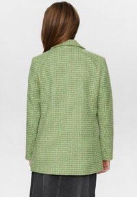 Grön texturerad blazer med rutmönster, flikiga slag och l�ånga ärmar. Baksidan har en något rundad nederkant.
