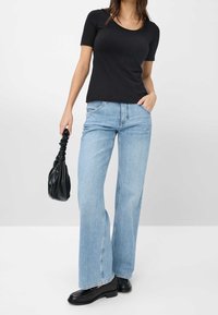 T-shirt nero aderente, jeans a gamba larga blu chiaro, mocassini neri spessi e una clutch nera arricciata. Design semplice con texture di tessuto morbide.