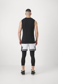 Haut sans manches noir, shorts en mesh blancs avec des accents noirs, et leggings noirs. Baskets noires avec un logo. Vu de l'arrière.