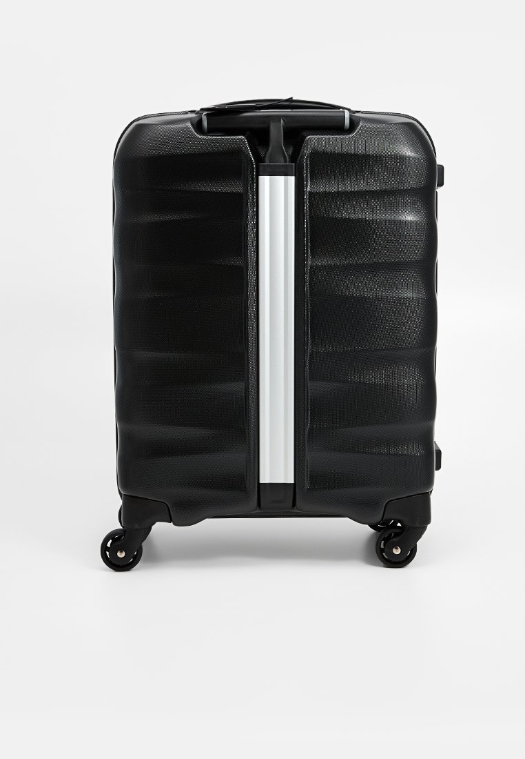 Valise rigide noire avec surface texturée, zip argenté et quatre roues pour la mobilité. Dispose d'une poignée centrale pour une prise en main facile.
