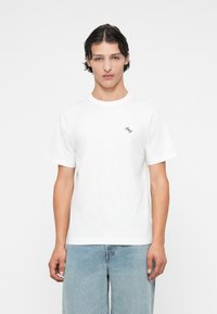 White cotton t-shirt with short sleeves, crew neck, featuring a small navy logo on the left chest. Smooth texture, relaxed fit.