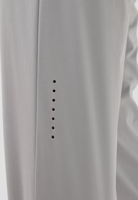 Lichtgrijze broek van een gladde stof met een verticale rij kleine gaatjes aan de zijkant voor ventilatie of als ontwerp.