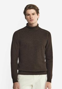 Mörkbrun polisongt tröja med ribbad krage och manschetter, med en mjuk textur och figurnära design, bärs över ljusa byxor.