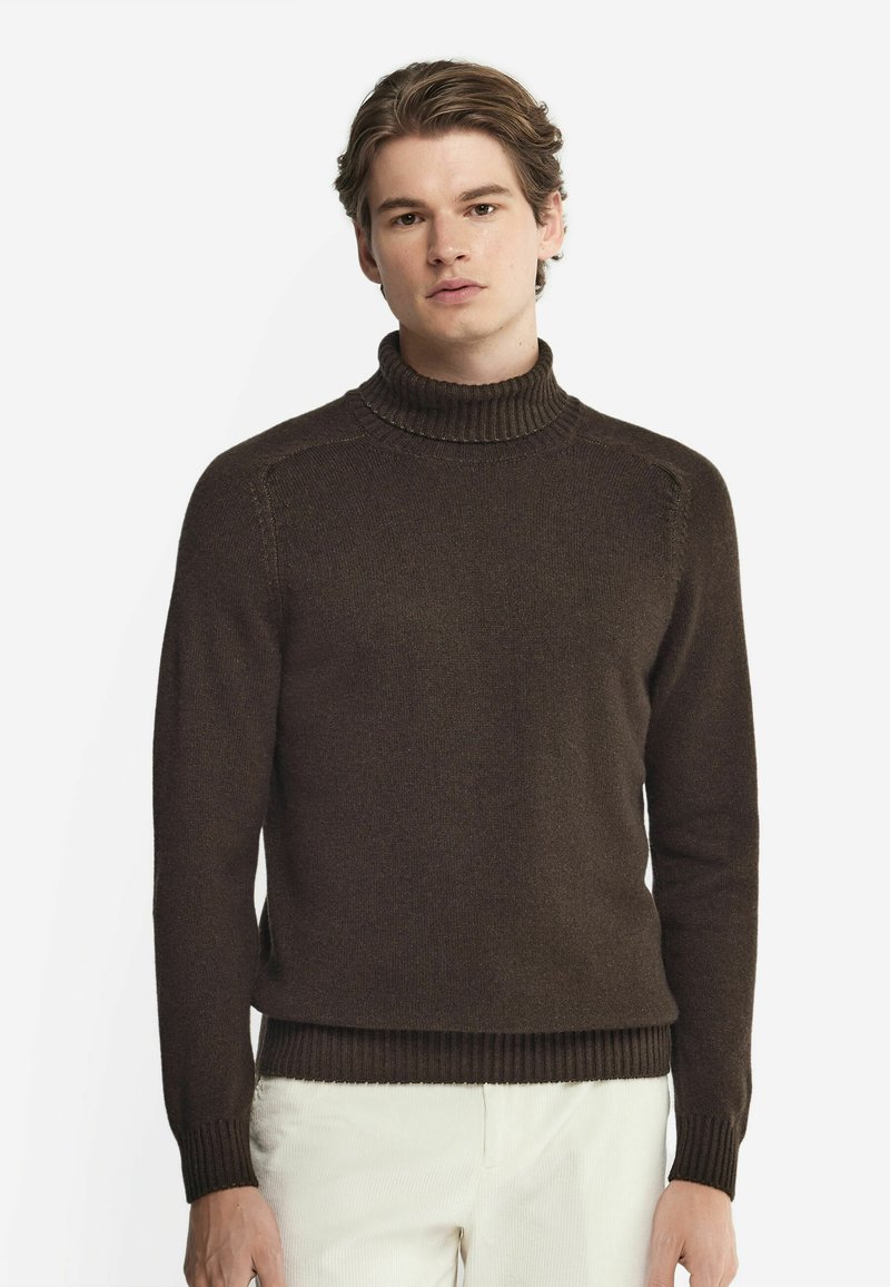 Mörkbrun polisongt tröja med ribbad krage och manschetter, med en mjuk textur och figurnära design, bärs över ljusa byxor.