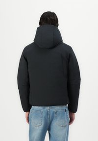 Black puffer jacket with a hood, featuring a smooth texture and modern design. Worn over light blue jeans, viewed from the back.