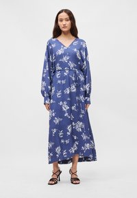 Μακρυμάνικο μπλε φόρεμα με λουλούδια, με V-κοπή, σφιχτή μέση και ζώνη. Φτιαγμένο από μαλακό ύφασμα με λευκά λουλουδάτα μοτίβα και ρέουσα σχεδίαση.