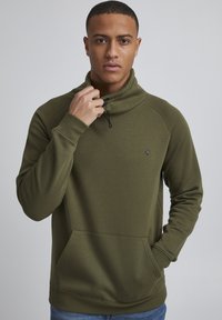 Felpa pullover verde oliva con alto colletto, chiusura a mezza zip e tasca frontale. Tessuto liscio con polsini e orlo a coste.