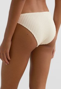 Kremowe majtki bikini o fakturze przypominającej wafelek i wysokim stanem. Gładki materiał z delikatnym połyskiem, minimalne krycie.