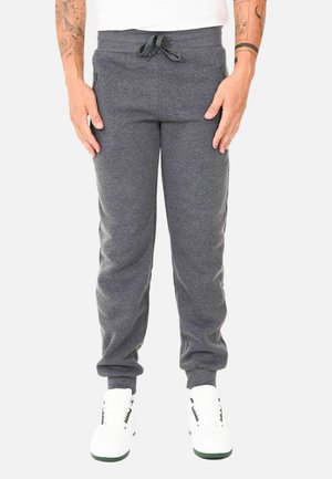 Pantaloni sportivi grigi in un tessuto morbido, con vita a coulisse, tasche laterali e polsini a costine, abbinati a sneakers bianche.