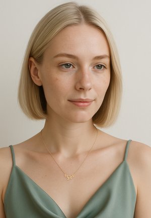 Guldbelagt design halskæde på en delikat kæde, båret over en grøn satin top. Glat overflade og sammenflettede bladlegeringer.
