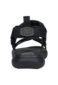 Sandale noire avec des sangles réglables, une semelle texturée et une semelle robuste. Présente un logo sur la sangle. Idéale pour un usage décontracté.