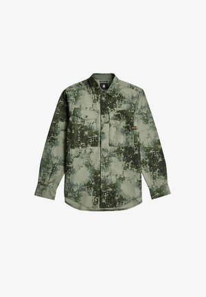 Chemise à manches courtes avec boutons dans un motif de camouflage en pixels verts. Comprend deux poches poitrine et un ourlet arrondi. Matière en coton.