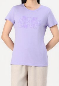 Fialové bavlněné tričko s kulatým výstřihem a krátkými rukávy, zdobené květinovým vzorem a písmeny "GAP" v kontrastní barvě.